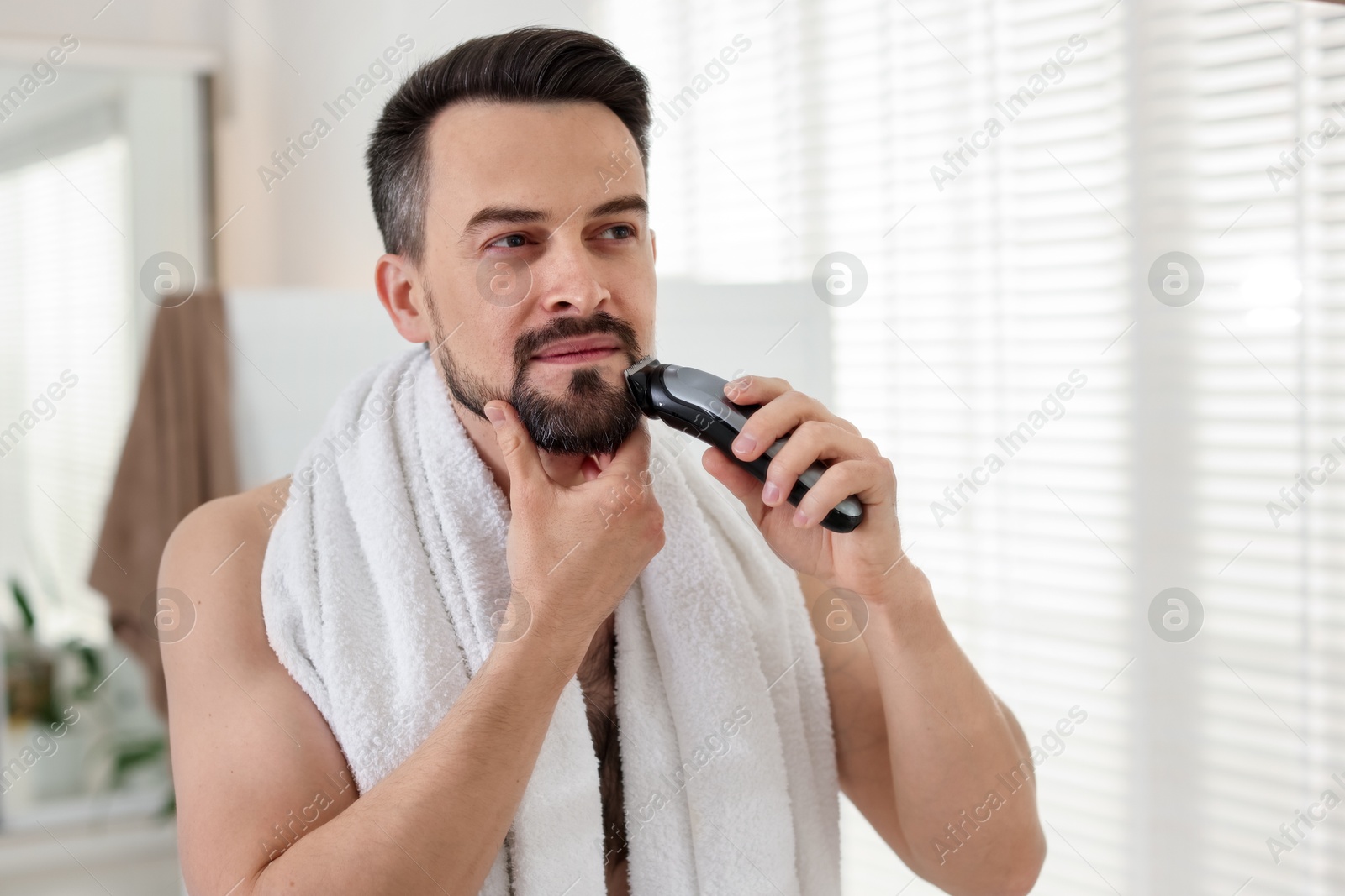 Photo of Handsome man shaving with trimmer at home