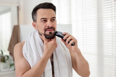 Photo of Handsome man shaving with trimmer at home