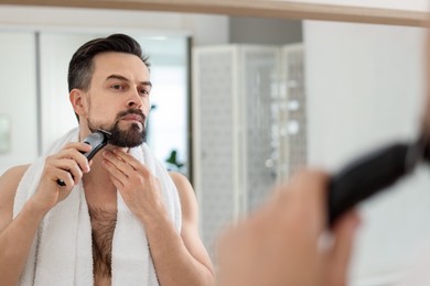 Photo of Handsome man shaving with trimmer near mirror at home