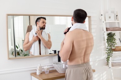Photo of Handsome man shaving with trimmer near mirror in bathroom