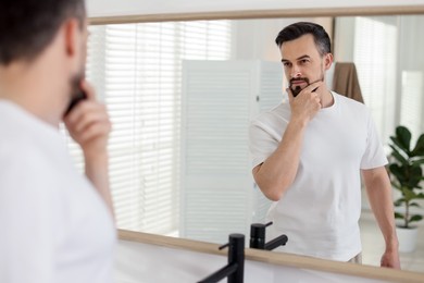 Photo of Handsome man before shaving looking at mirror in bathroom