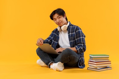 Photo of Student with headphones and laptop on orange background
