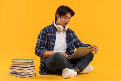 Photo of Student with headphones and laptop on orange background