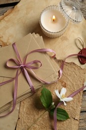 Photo of Stack of love letters, flower, candle and parchment sheets on wooden table, flat lay