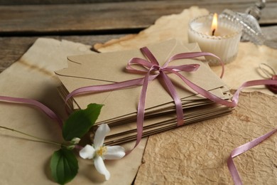 Photo of Stack of love letters, flower, candle and parchment sheets on wooden table, closeup
