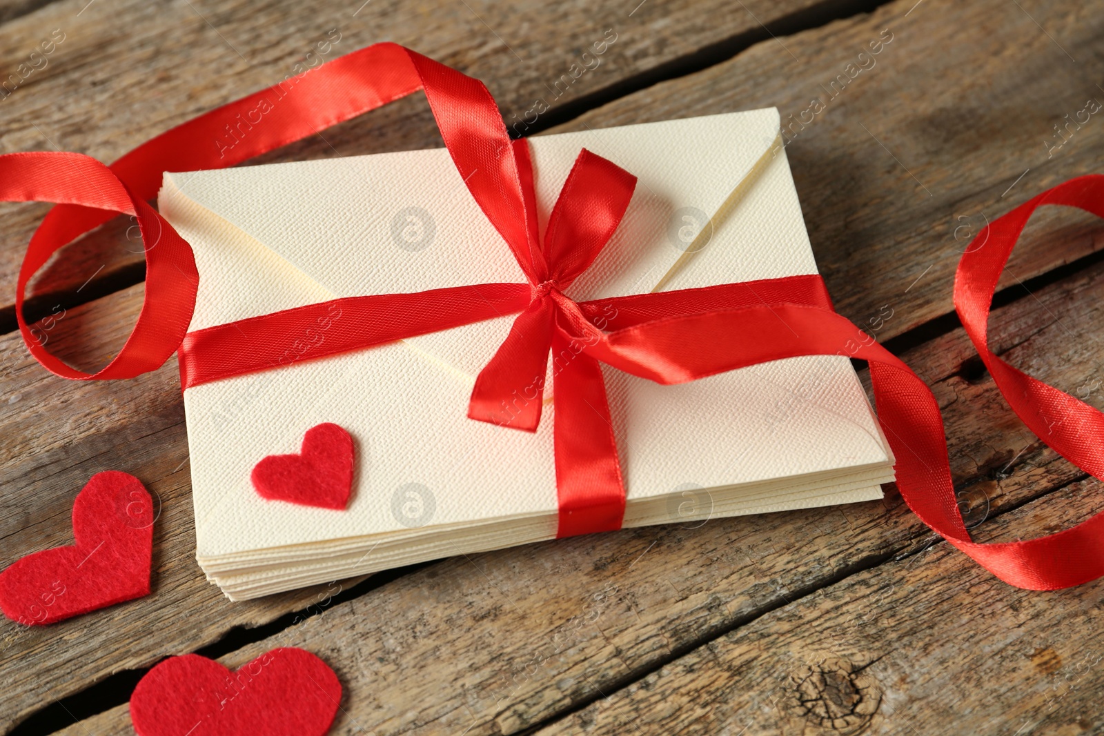 Photo of Stack of love letters and paper hearts on wooden table, closeup
