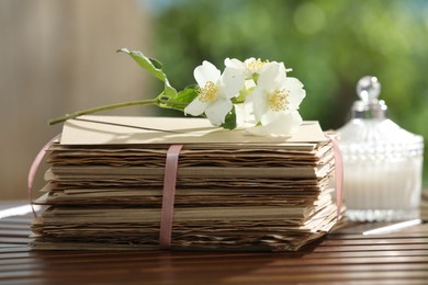 Photo of Stack of love letters and flowers on wooden table, closeup