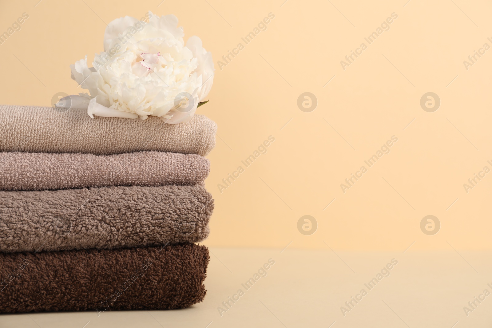 Photo of Stack of towels and peony flower on beige background, closeup. Space for text