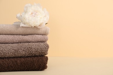 Photo of Stack of towels and peony flower on beige background, closeup. Space for text