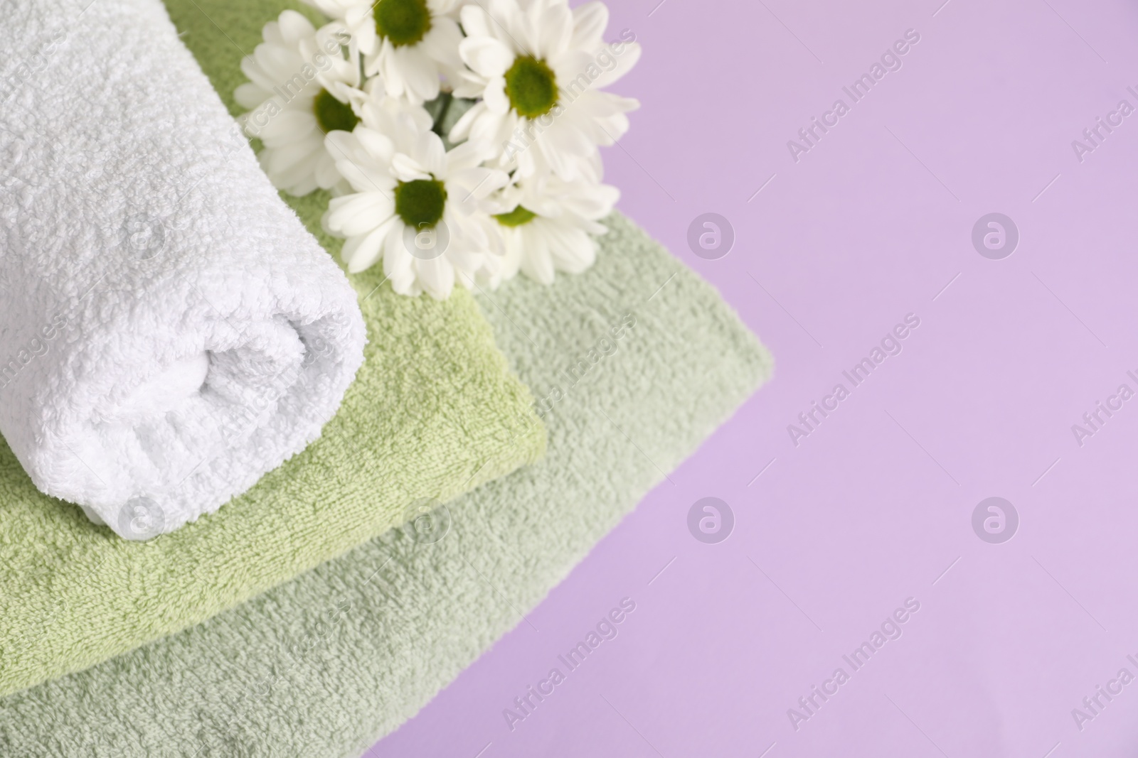 Photo of Soft towels and chrysanthemum flowers on violet background, above view. Space for text