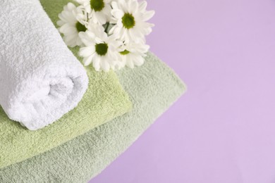 Photo of Soft towels and chrysanthemum flowers on violet background, above view. Space for text