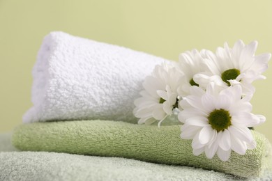 Photo of Soft towels and chrysanthemum flowers on pale green background, closeup