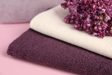 Photo of Soft towels and lilac flowers on pink background, closeup