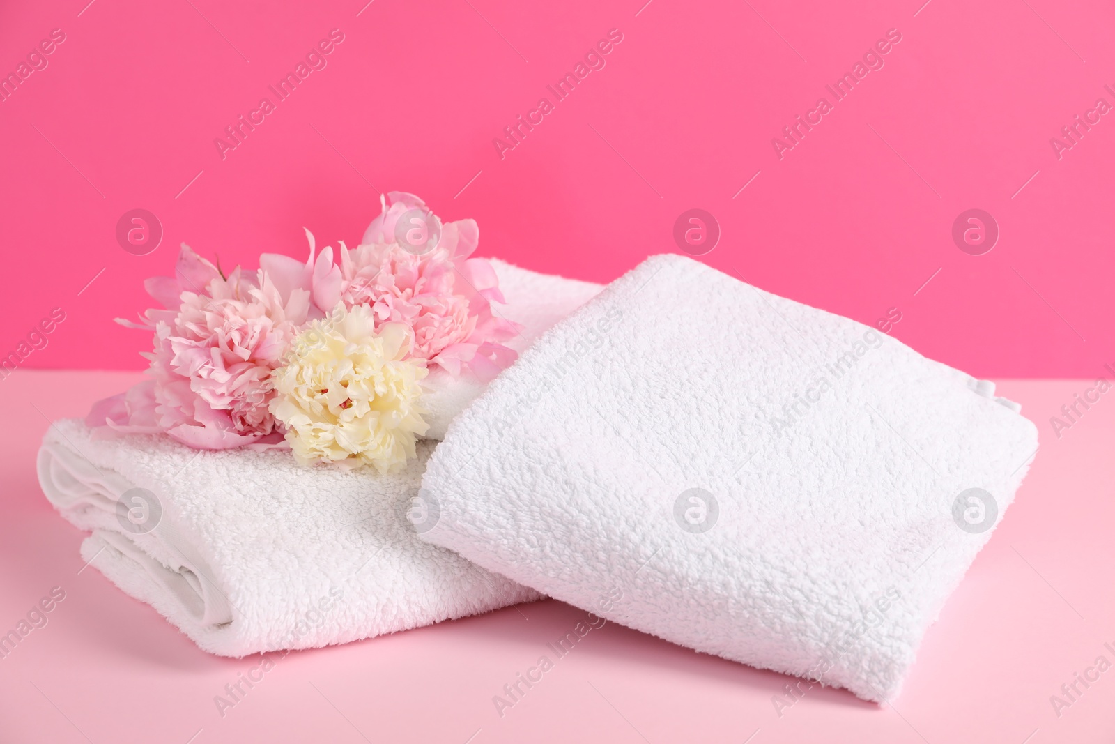Soft towels and peony flowers on pink background Photo of Soft towels and peony flowers on pink background