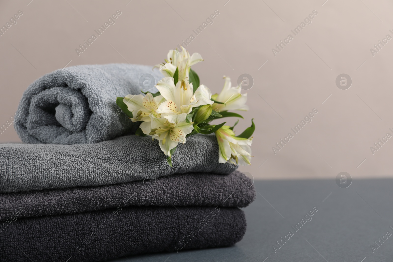 Soft towels and lilies on grey table against beige background, closeup. Space for text Photo of Soft towels and lilies on grey table against beige background, closeup. Space for text