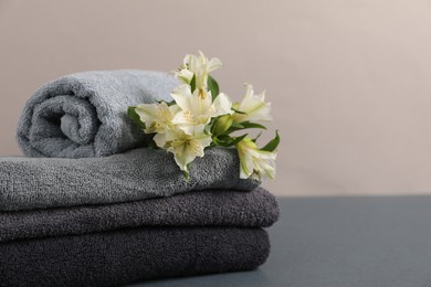 Photo of Soft towels and lilies on grey table against beige background, closeup. Space for text