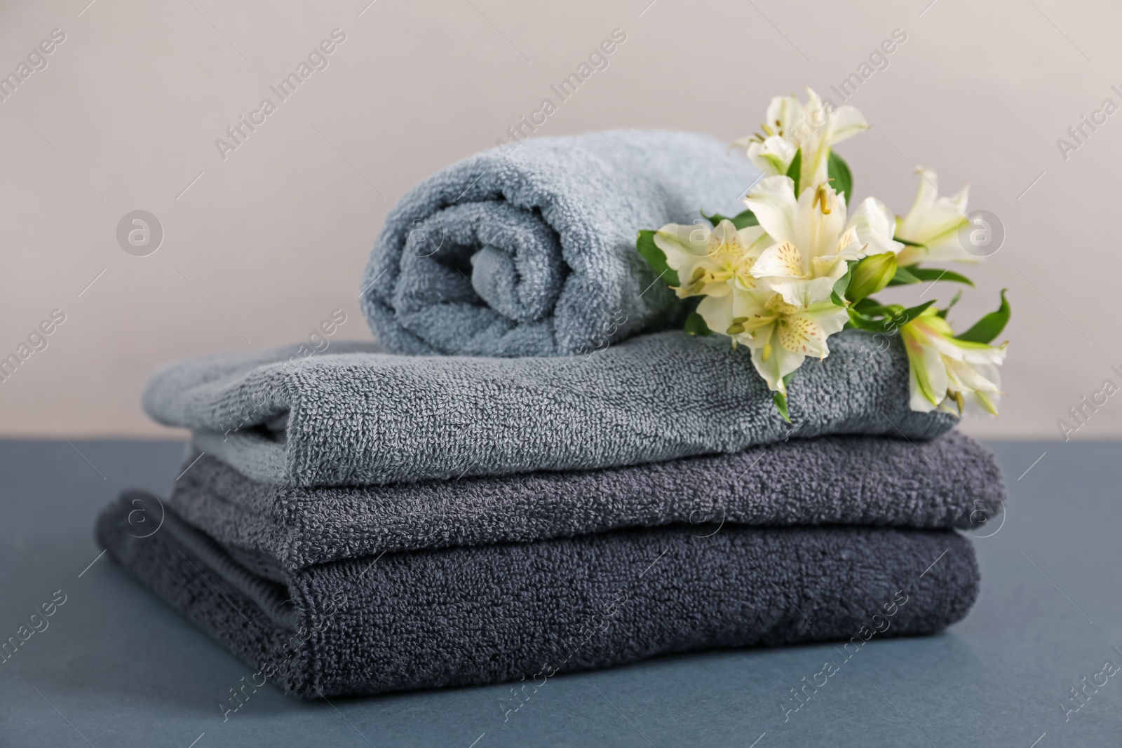 Soft towels and lilies on grey table against beige background, closeup Photo of Soft towels and lilies on grey table against beige background, closeup