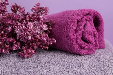 Photo of Soft towels and lilac flowers on violet background, closeup