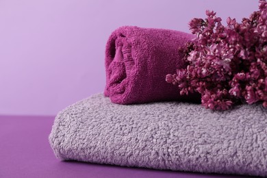 Photo of Soft towels and lilac flowers on color background, closeup