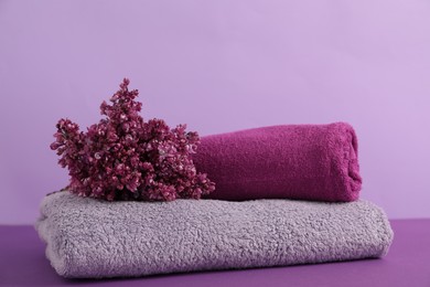 Photo of Soft towels and lilac flowers on color background, closeup