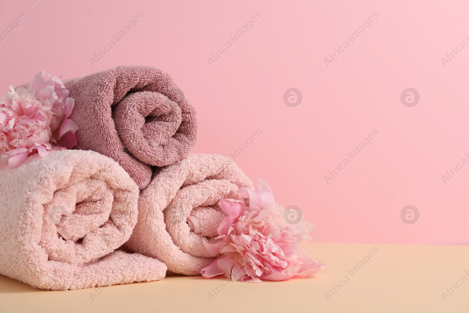 Soft towels and peony flowers on beige table against pink background, closeup. Space for text Photo of Soft towels and peony flowers on beige table against pink background, closeup. Space for text