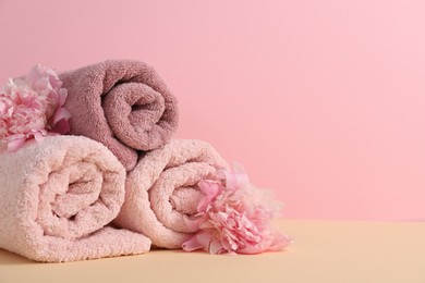 Photo of Soft towels and peony flowers on beige table against pink background, closeup. Space for text