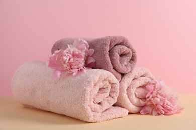 Photo of Soft towels and peony flowers on beige table against pink background, closeup