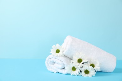 Photo of Soft towels and chrysanthemum flowers on light blue background, space for text