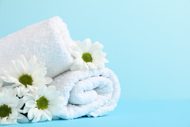 Photo of Soft towels and chrysanthemum flowers on light blue background, closeup. Space for text