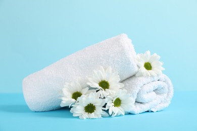 Photo of Soft towels and chrysanthemum flowers on light blue background