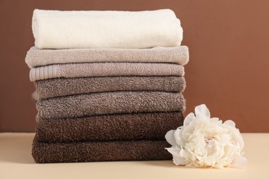 Photo of Stack of towels and peony flower on beige table against brown background