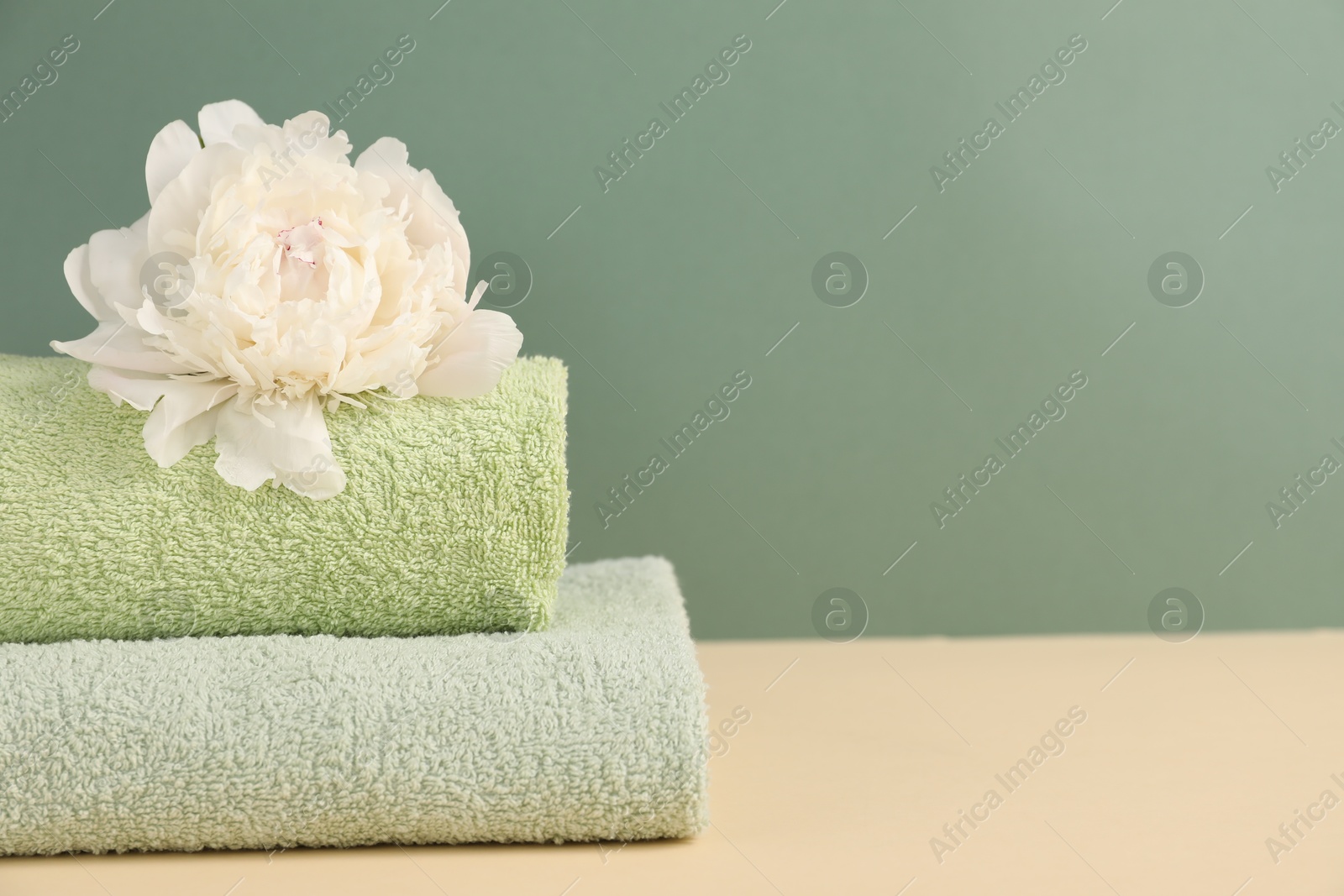Soft towels and peony flower on beige table against green background, closeup. Space for text Photo of Soft towels and peony flower on beige table against green background, closeup. Space for text