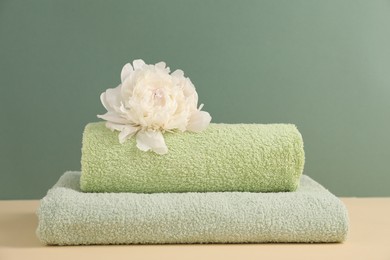 Photo of Soft towels and peony flower on beige table against green background