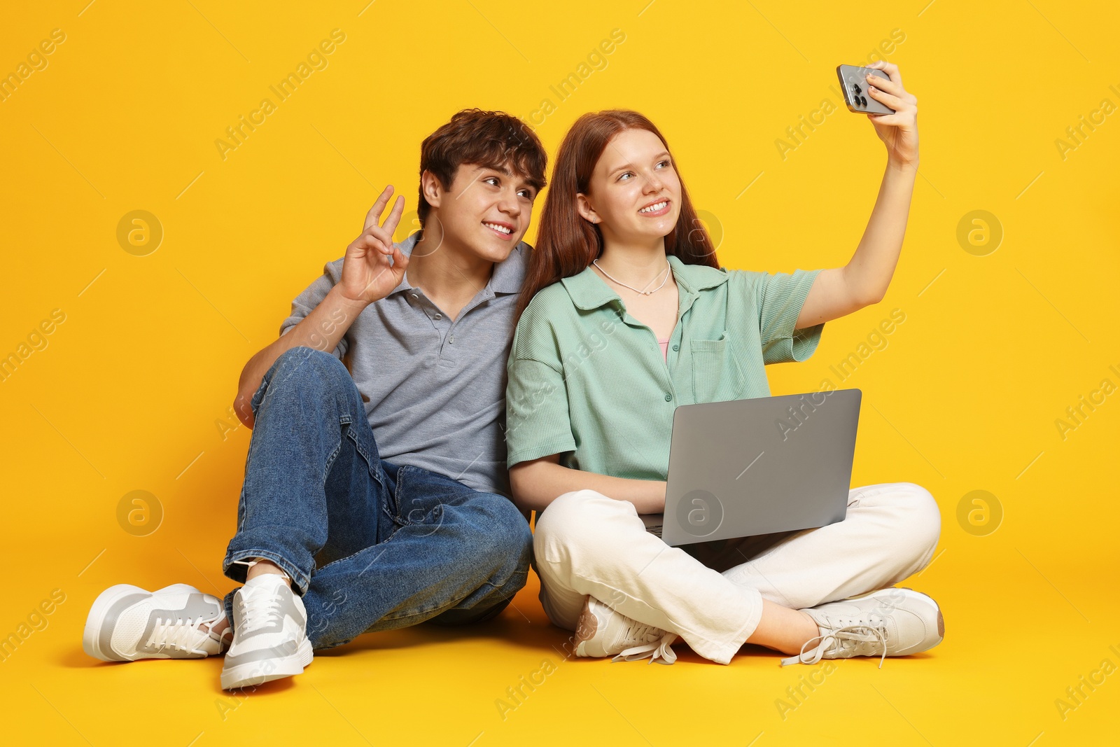 Teenage girl and boy with laptop taking selfie on yellow background Photo of Teenage girl and boy with laptop taking selfie on yellow background