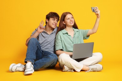 Photo of Teenage girl and boy with laptop taking selfie on yellow background