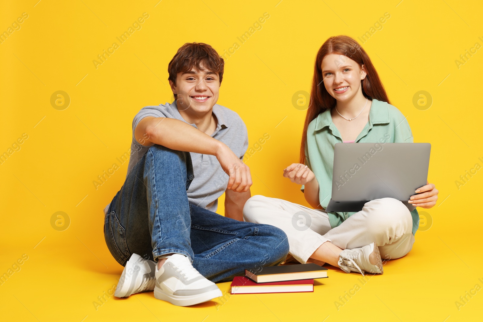 Teenage girl and boy with laptop on yellow background Photo of Teenage girl and boy with laptop on yellow background
