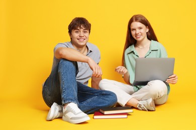 Photo of Teenage girl and boy with laptop on yellow background
