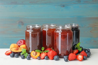 Photo of Different jams in jars and ingredients on white table. Space for text