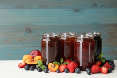 Photo of Different jams in jars and ingredients on white table. Space for text