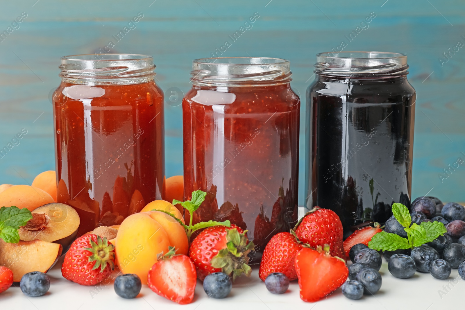 Different jams in jars and ingredients on white table, closeup Photo of Different jams in jars and ingredients on white table, closeup