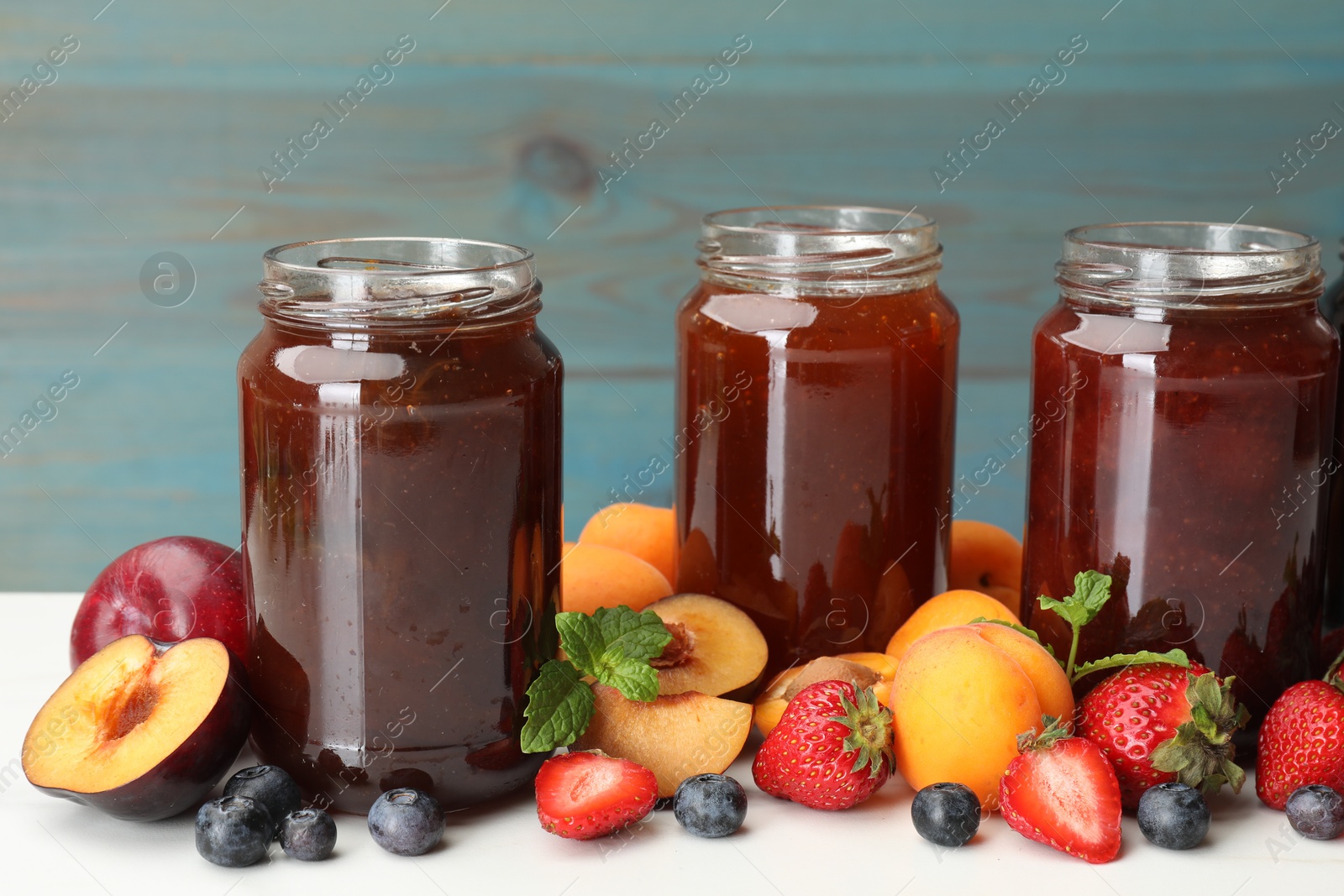 Different jams in jars and ingredients on white table, closeup Photo of Different jams in jars and ingredients on white table, closeup