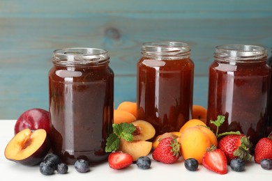 Photo of Different jams in jars and ingredients on white table, closeup