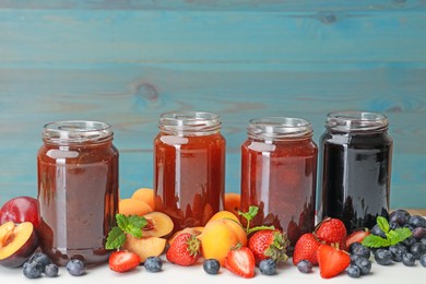 Photo of Different jams in jars and ingredients on white table. Space for text
