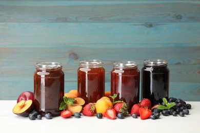 Photo of Different jams in jars and ingredients on white table. Space for text