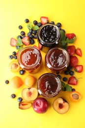 Photo of Different jams in jars and ingredients on yellow background, flat lay