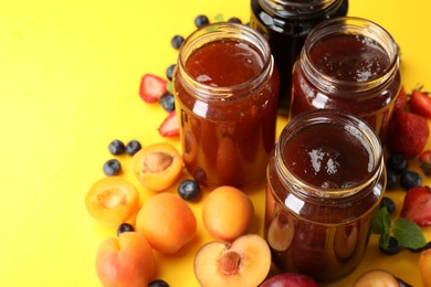 Photo of Different jams in jars and ingredients on yellow background, closeup