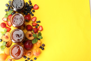 Photo of Different jams in jars and ingredients on yellow background, flat lay. Space for text