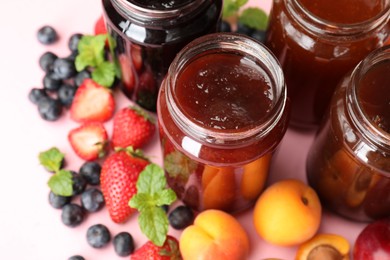 Photo of Different jams in jars and ingredients on light pink background, closeup