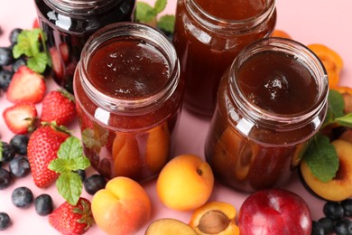 Photo of Different jams in jars and ingredients on light pink background, closeup