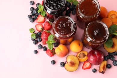 Photo of Different jams in jars and ingredients on light pink background, flat lay